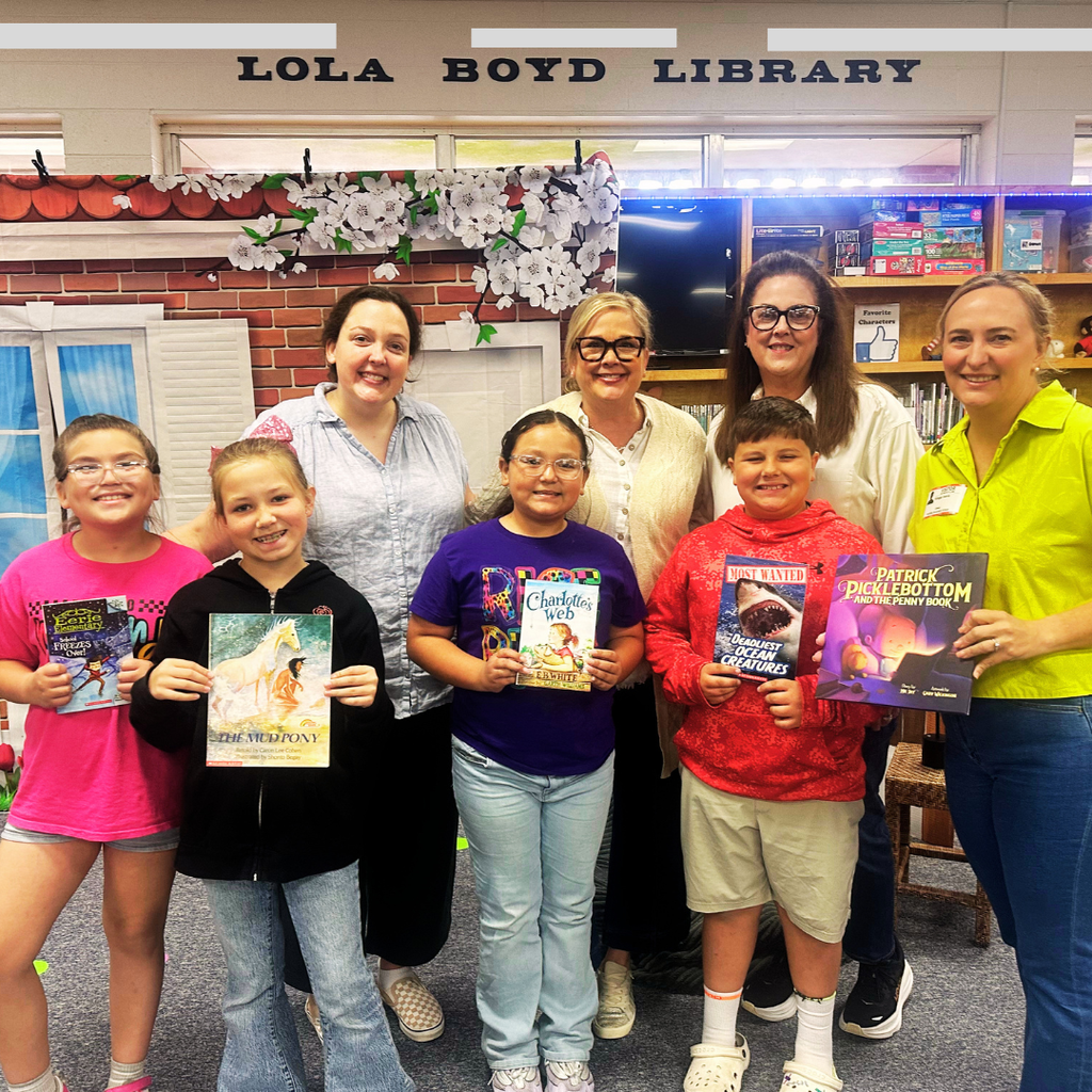 Four Hutchins students and four adults stand together in the Lola Boyd Library, proudly holding up new books during a Reading Is Fundamental (RIF) event.