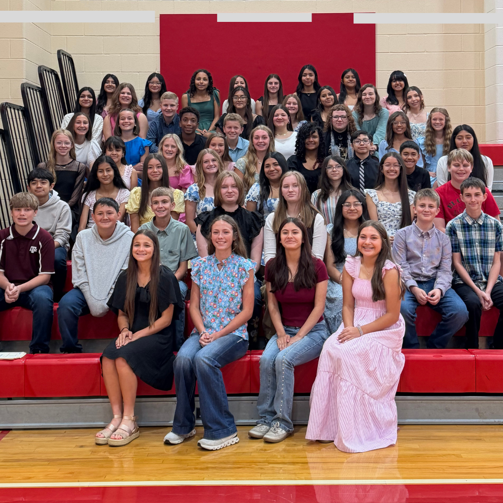 A large group of El Campo Middle School students sitting on red bleachers in a gymnasium. The students are the 2026-2027 National Junior Honor Society inductees, smiling and dressed in semi-formal attire for their induction ceremony.