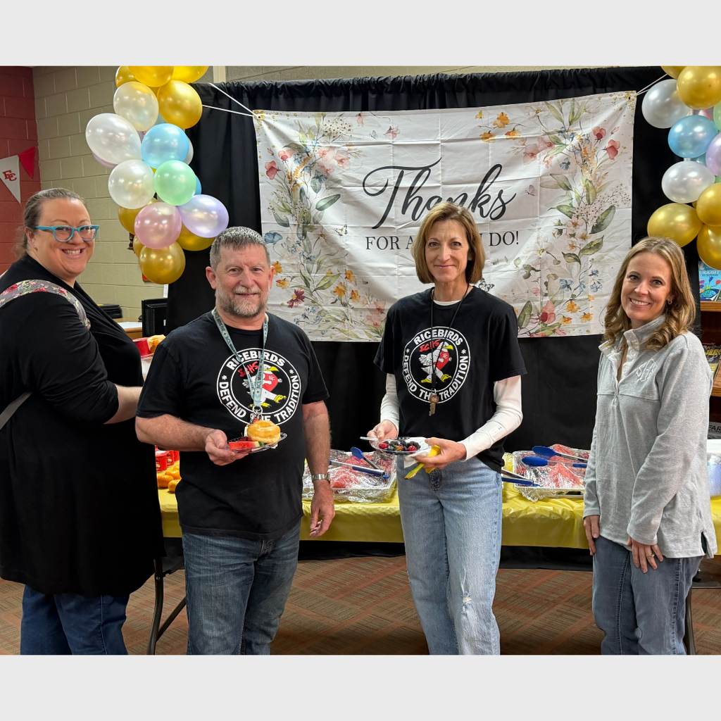 Four staff members posing together in front of a floral "Thanks for all you do!" banner. Two individuals in the center are holding plates of breakfast food, including donuts. The scene is decorated with blue, gold, and white balloons to celebrate Teacher Appreciation Week.