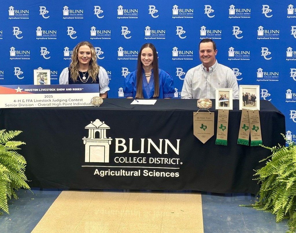 ECHS student Ashlyn Peters sits at a decorated Blinn College Agricultural Sciences table, flanked by two college representatives. The background features a Blinn College repeat banner, and the table displays her livestock judging awards."