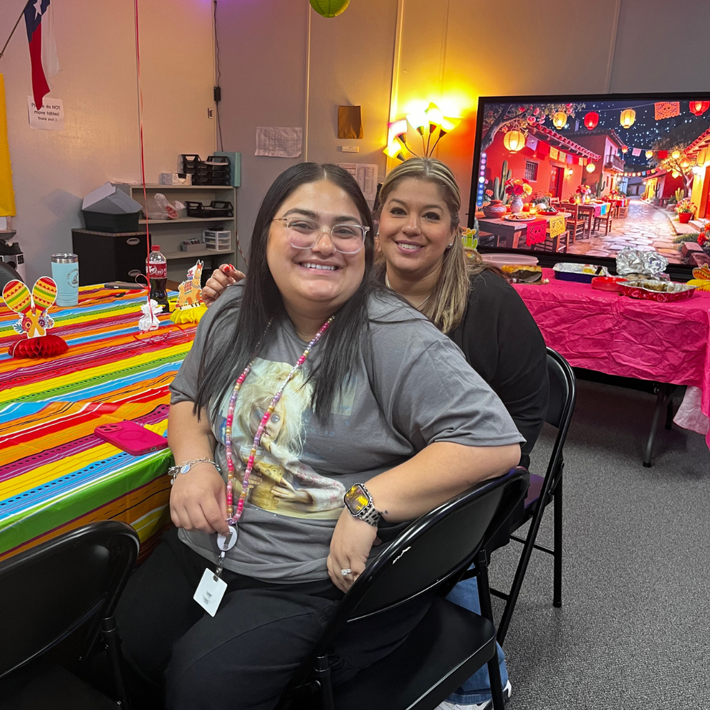 Two staff members smiling and posing together during the taco luncheon in a decorated classroom.