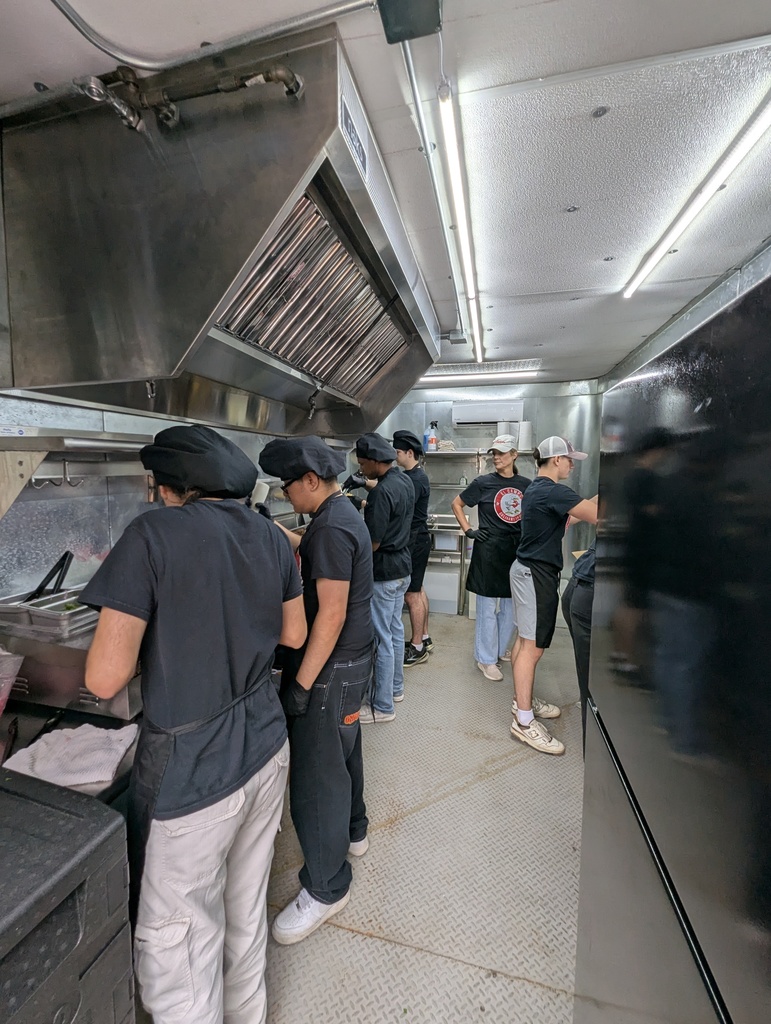 Culinary arts students working inside the kitchen of "The Bird Feeder" food truck, preparing meals for faculty and staff.