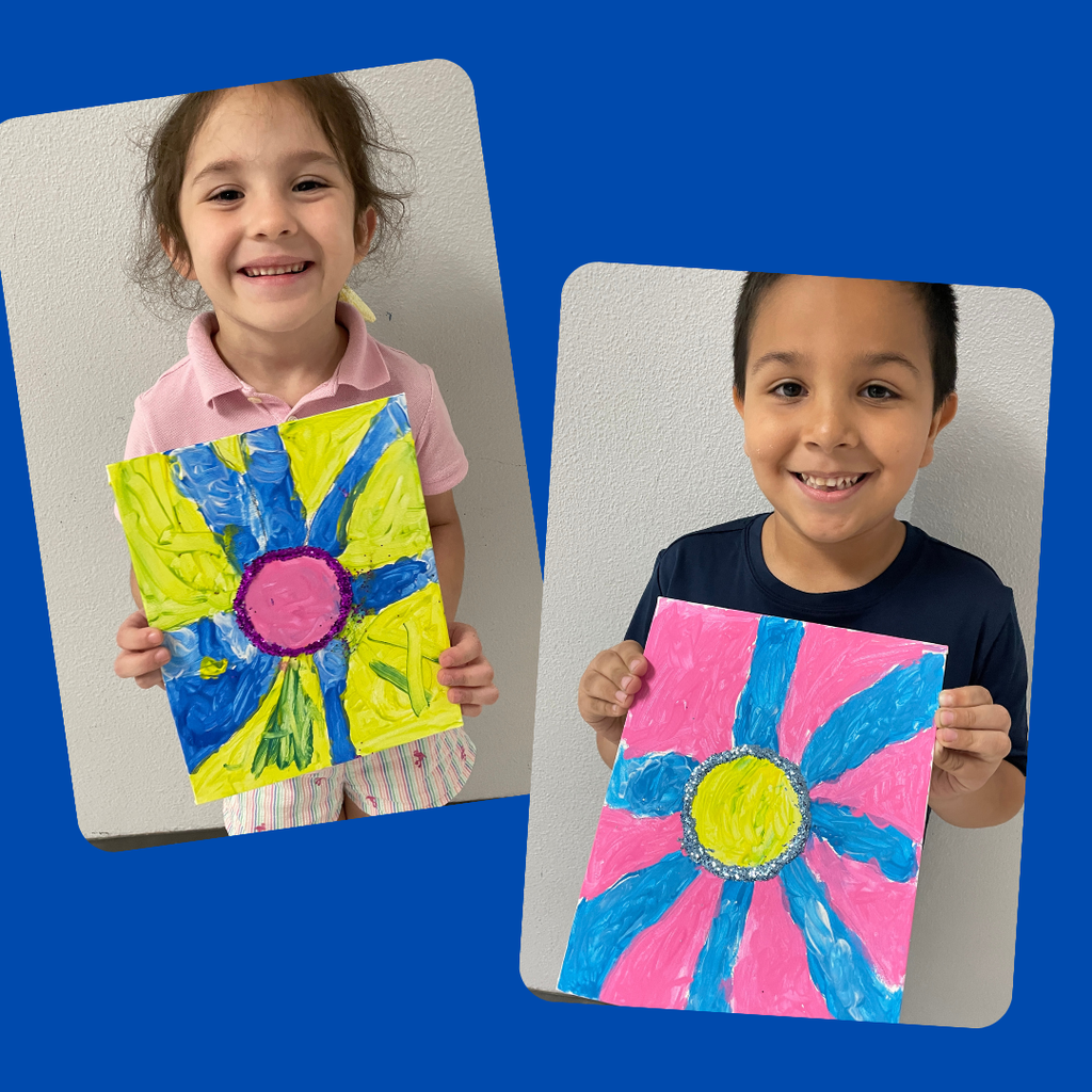kindergarten students stand together smiling and holding up their colorful, hand-painted flower artwork. The students are each proudly displaying a unique bluebonnet-inspired painting featuring vibrant petals and bright backgrounds.