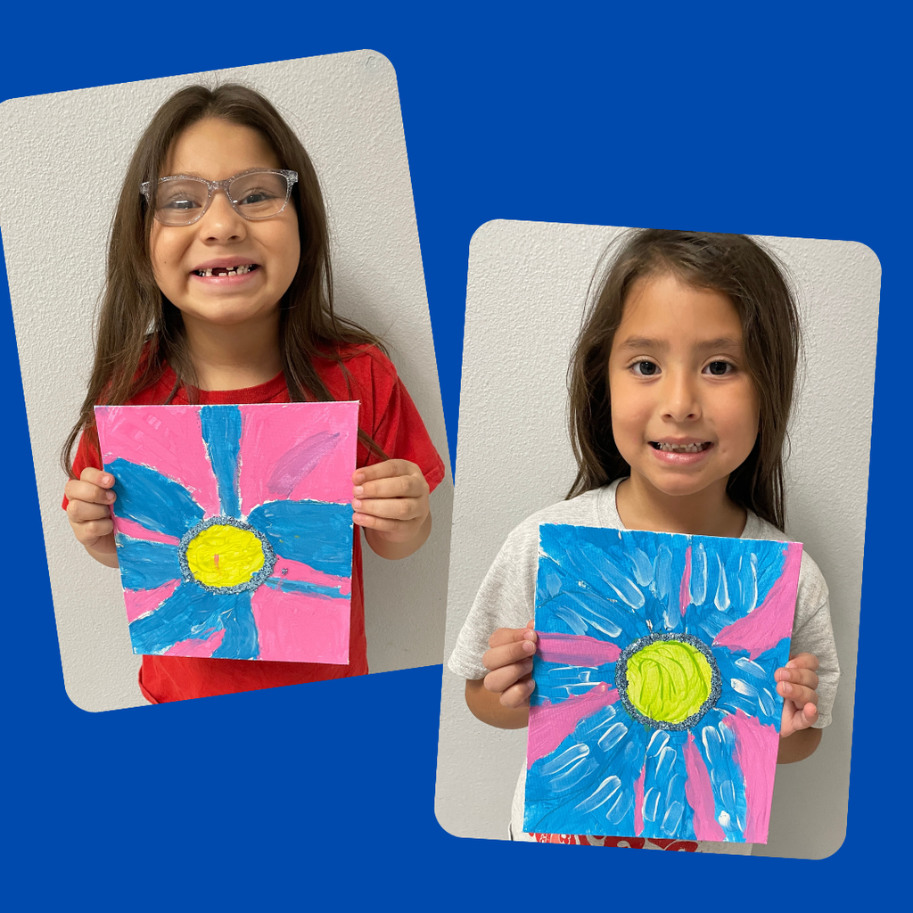 kindergarten students stand together smiling and holding up their colorful, hand-painted flower artwork. The students are each proudly displaying a unique bluebonnet-inspired painting featuring vibrant petals and bright backgrounds.