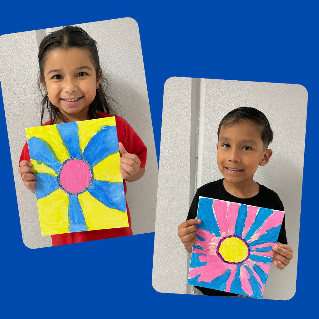 kindergarten students stand together smiling and holding up their colorful, hand-painted flower artwork. The students are each proudly displaying a unique bluebonnet-inspired painting featuring vibrant petals and bright backgrounds.