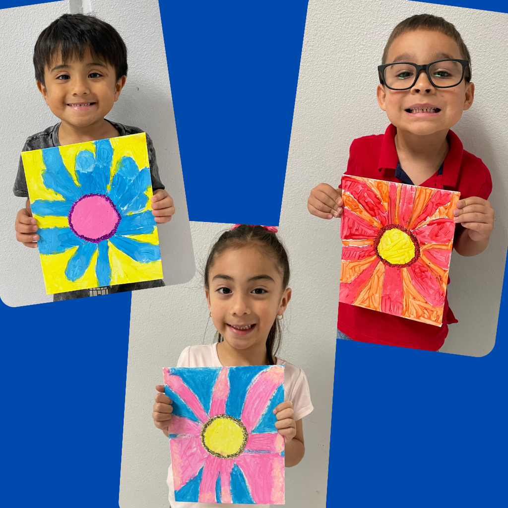 kindergarten students stand together smiling and holding up their colorful, hand-painted flower artwork. The students are each proudly displaying a unique bluebonnet-inspired painting featuring vibrant petals and bright backgrounds.