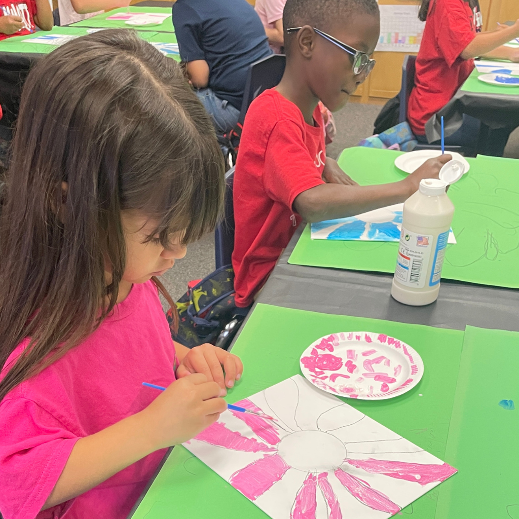 Kindergarten students at a table painting the petals on their piece of flower art