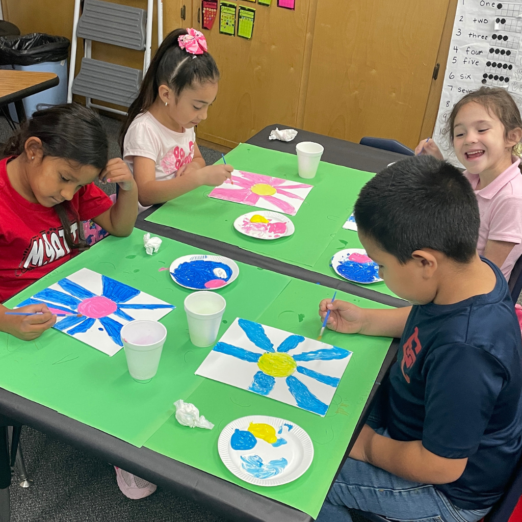 Kindergarten students at a table painting the background on their piece of flower art