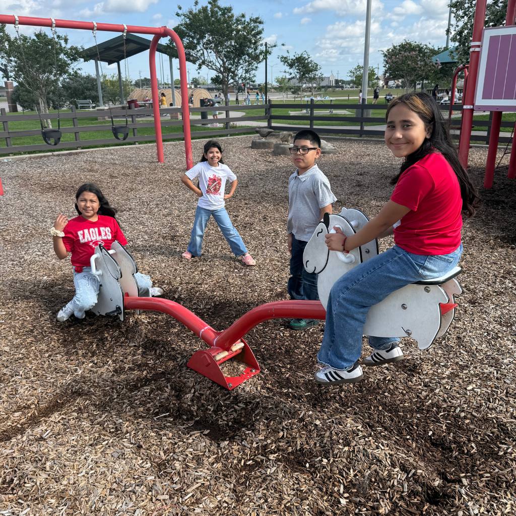 4 smiling 3rd-grade kids on the see saw at the park