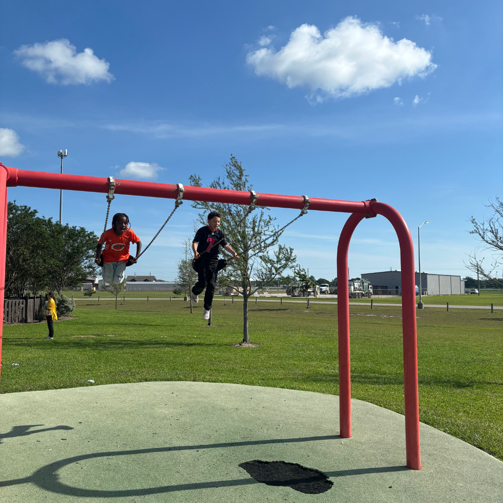 two smiling 3rd-grade kids swinging at the park