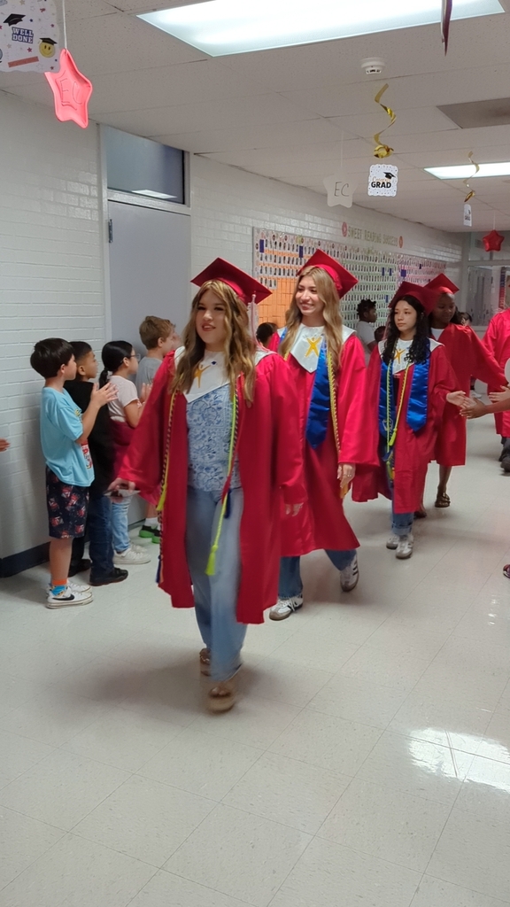 3 girls in their graduation gowns and caps walking the halls of an elementary campus