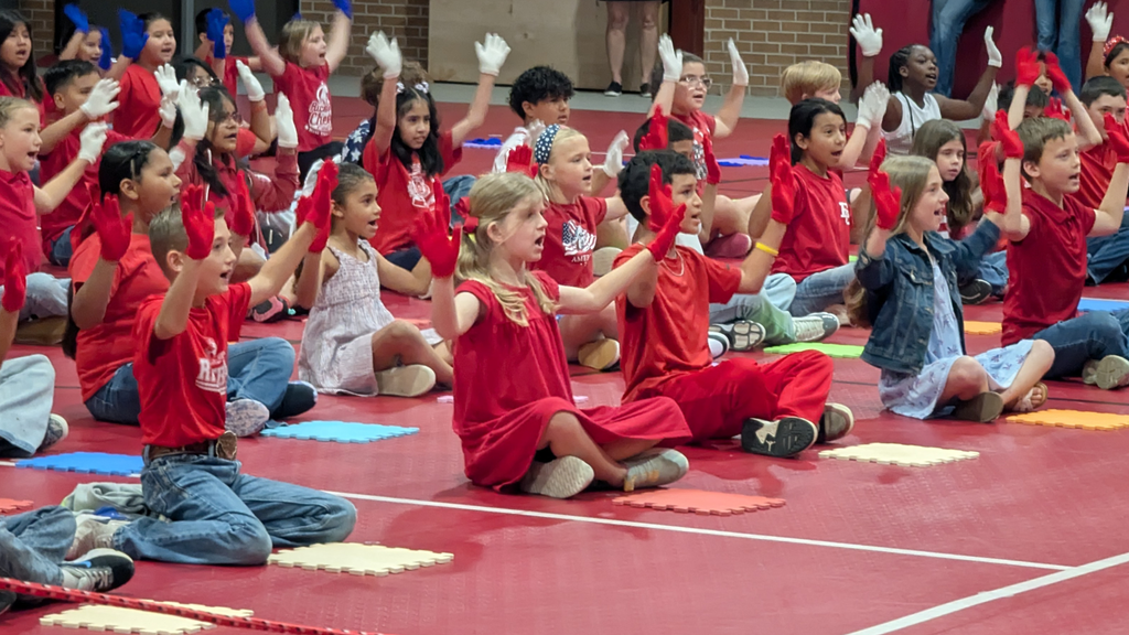 students on floor performing a song while wearing red, white, or blue gloves.