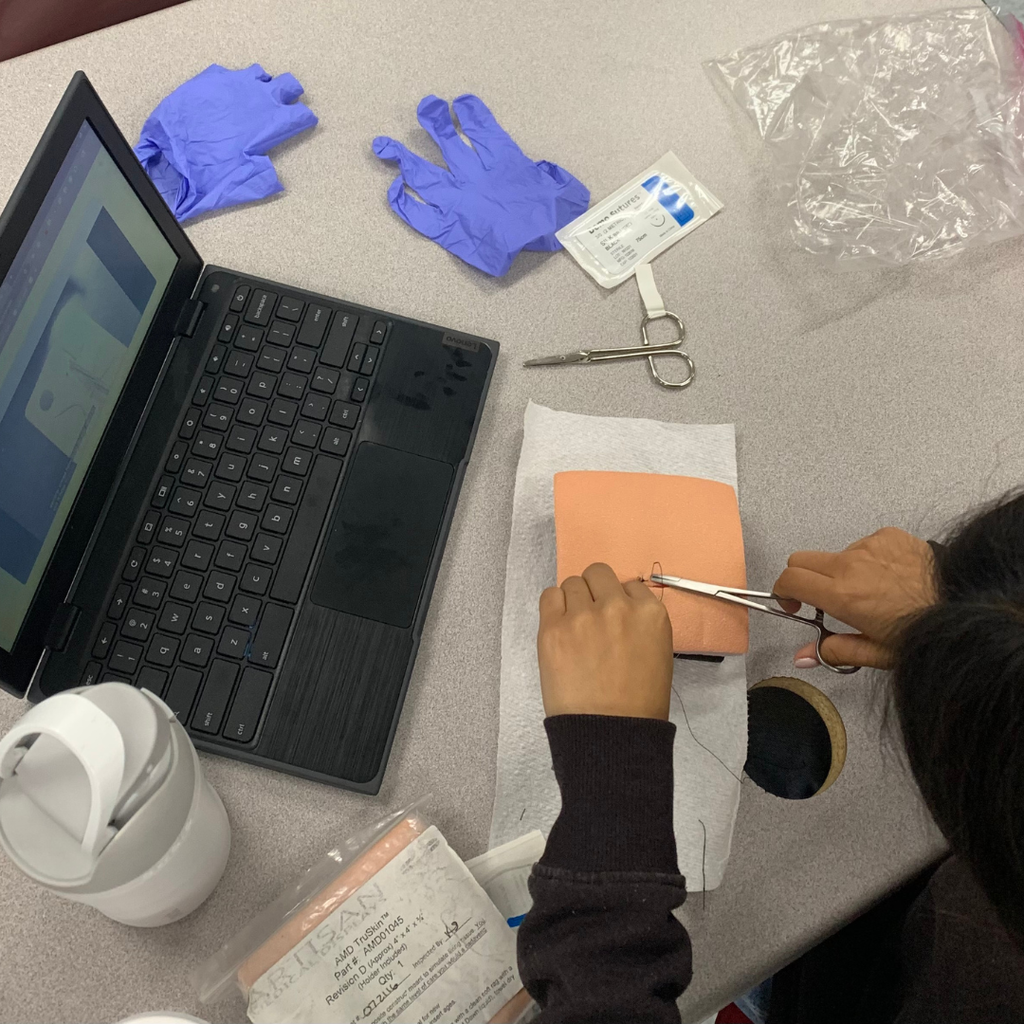 A student uses surgical tools to practice stitching a suture pad during a health science class.