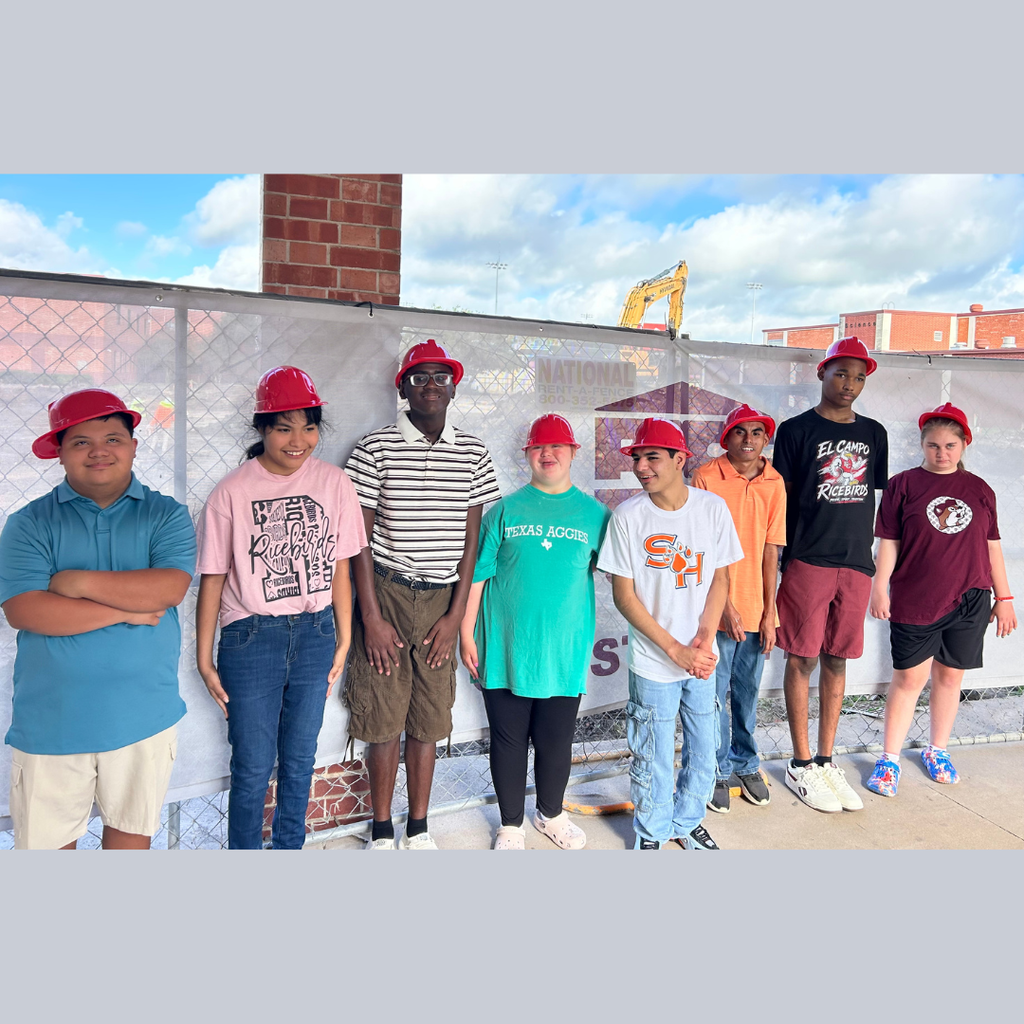 8 students in plastic hard hats with construction behind them