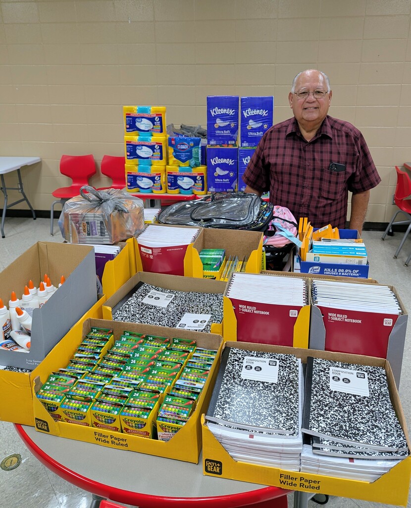 man surrounded by glue, crayons, spirals, composition books, and other various school supplies