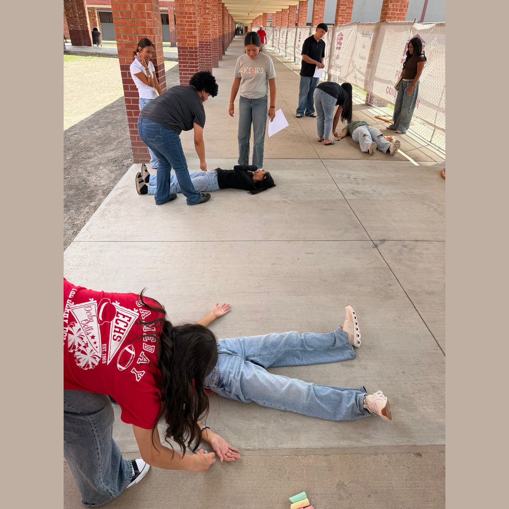 student traces the outline of another student lying on the concrete sidewalk