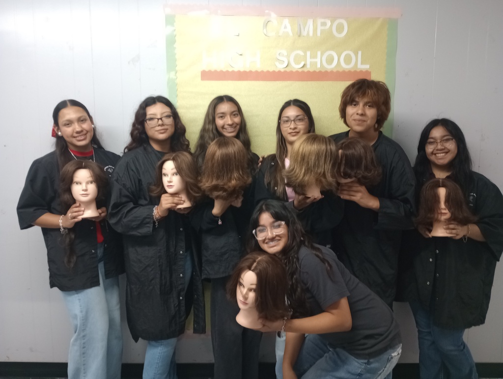 Cosmetology students posing together in their lab while holding styled mannequin heads.