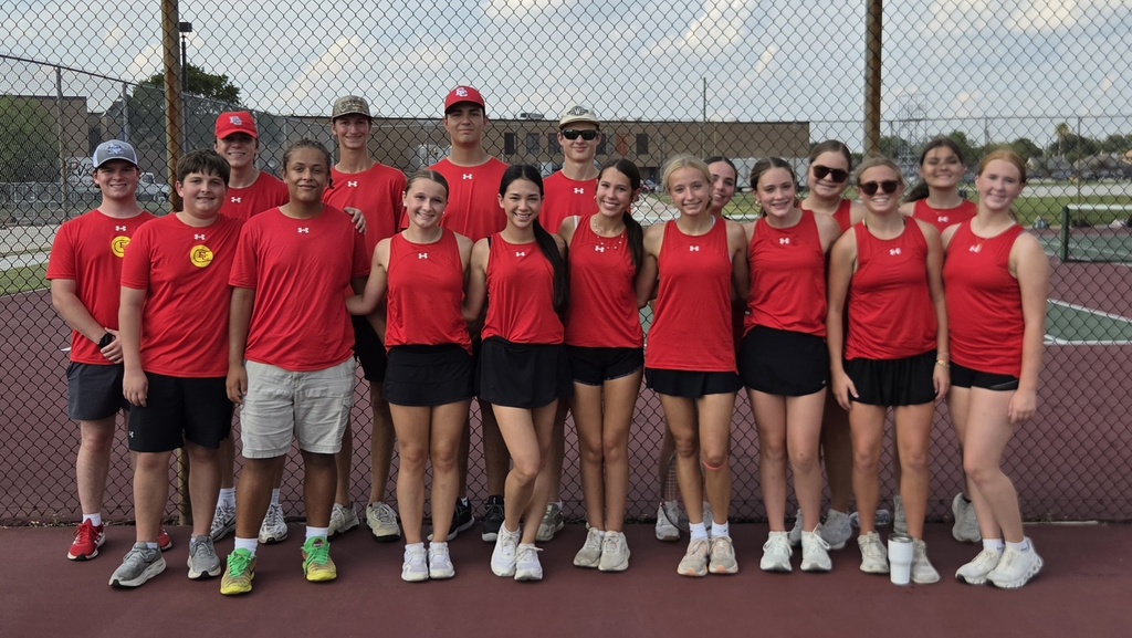 17 high schoolers in red shirts posing on the tennis court.
