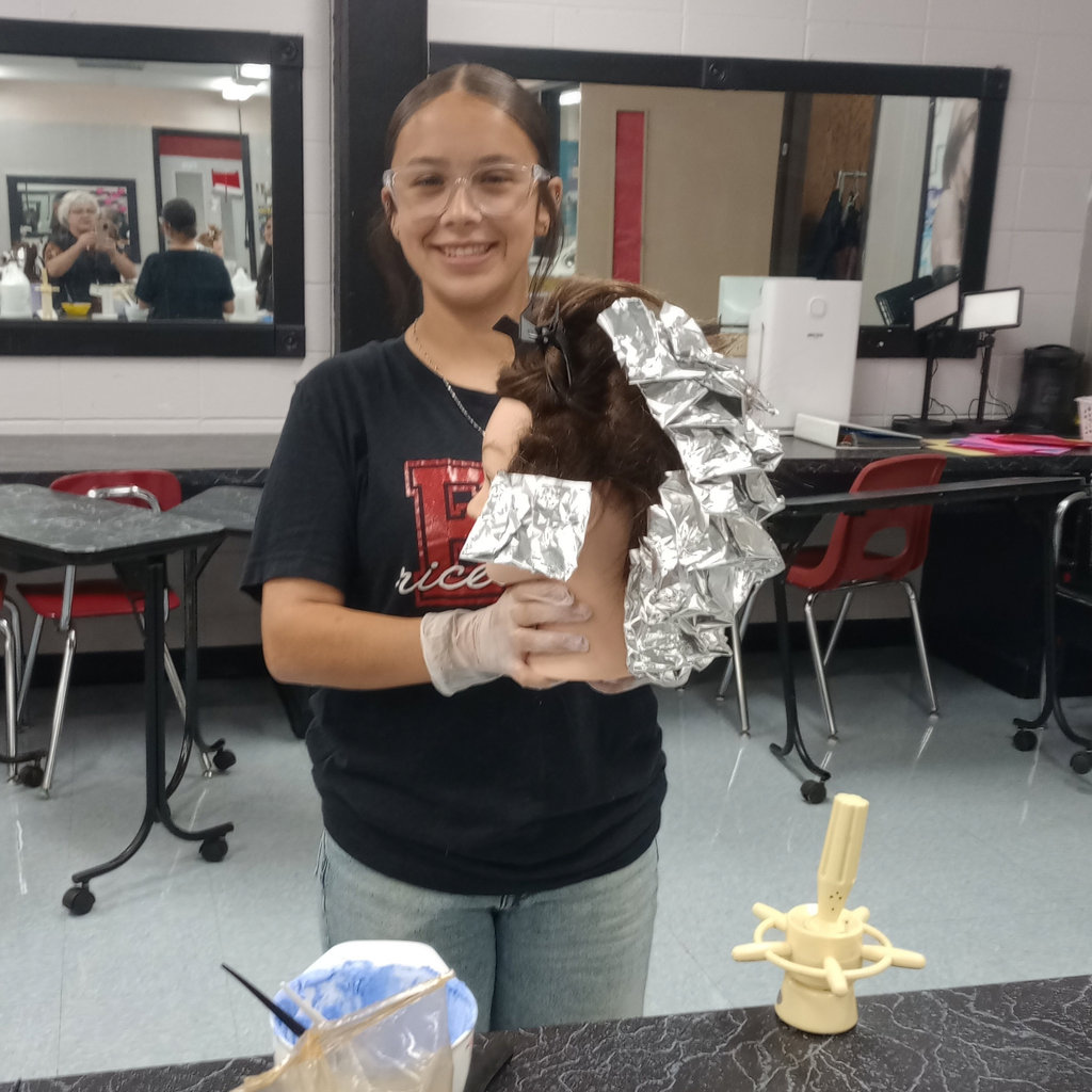 smiling student holding mannequin with hair in foil wraps
