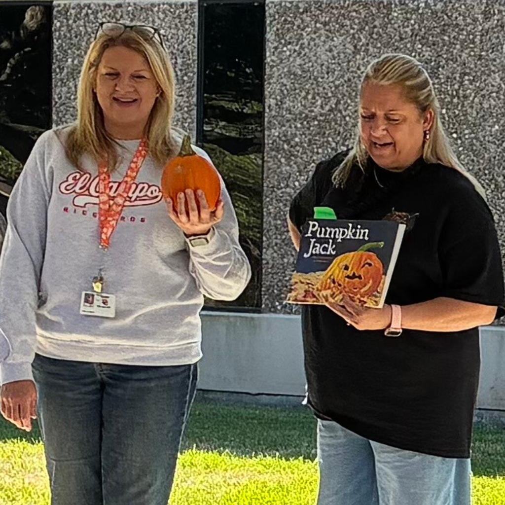Two teachers holding a small pumpkin and the children's book Pumpkin Jack outdoors.