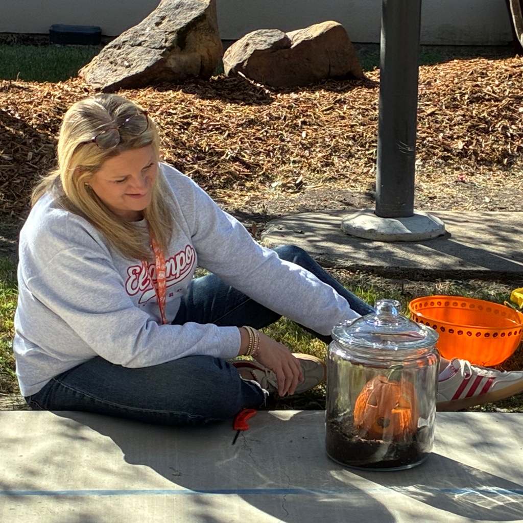 teacher looking at the freshly carved pumpkin sitting on the dirt in the clear jar