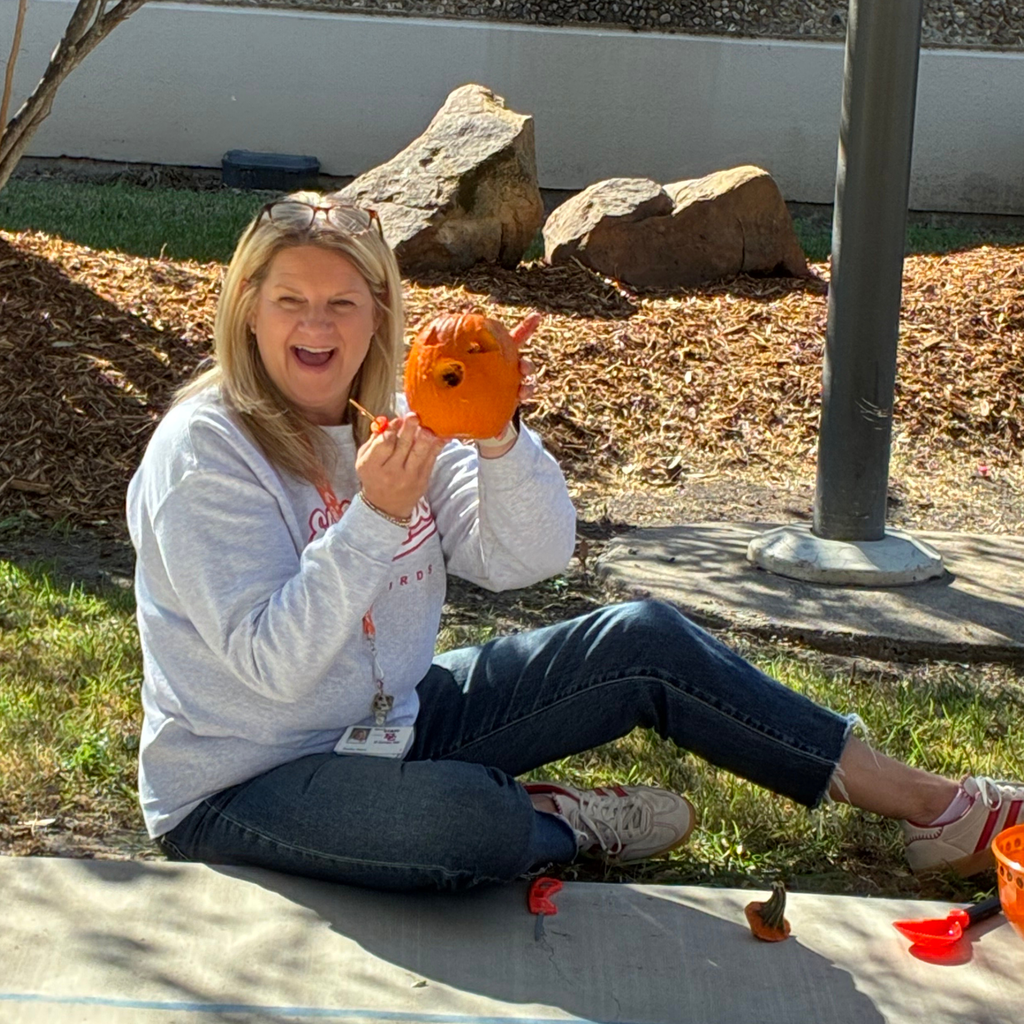 Teacher sitting outside holding a small carved jack-o'-lantern pumpkin.