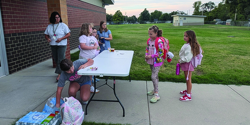 students stand at a table while two other students stand in line to purchase lemonade