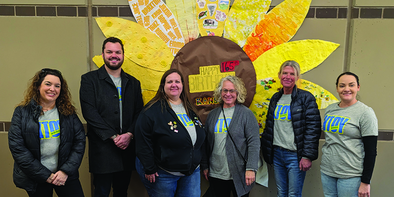The KTOY team poses in front of a giant paper sunflower