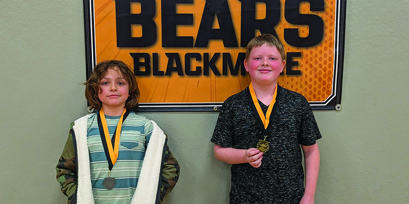 Blackmore spelling bee winner and runner-up pose with their medals in front of the Blackmore Bears banner