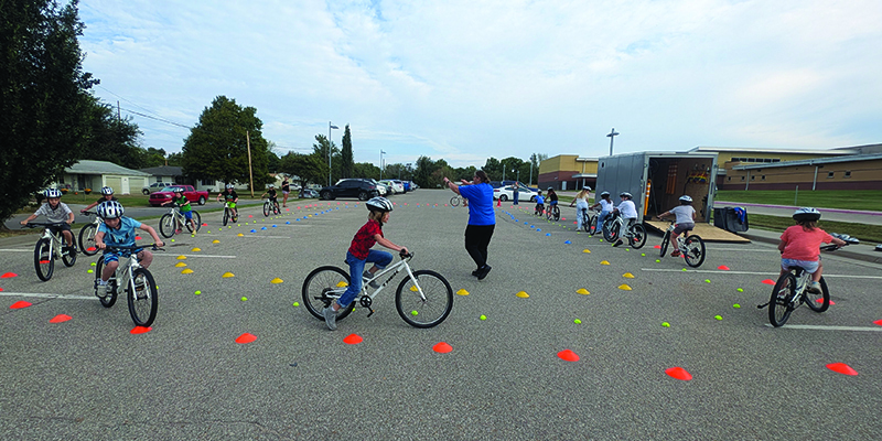 Students ride bicycles on a makred course in the parking lot