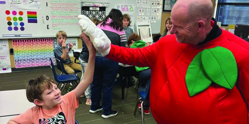 Russell Baker dressed as Papple gives a student sitting in a classroom a high five