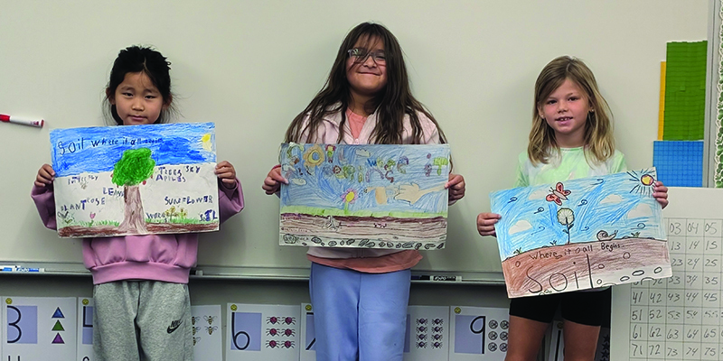three students hold hand-colored posters about soil conservation