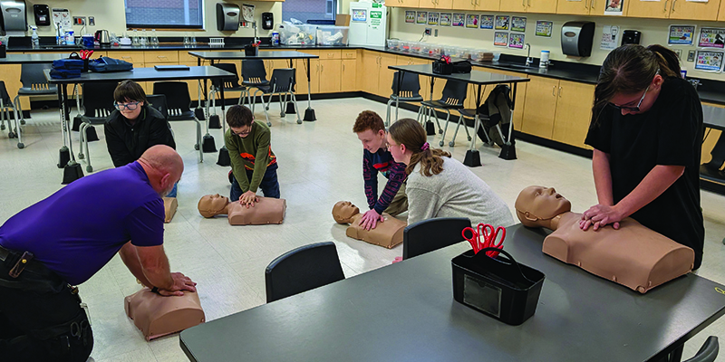 Students practice hands-only CPR on dummies with guidance from a paramedic