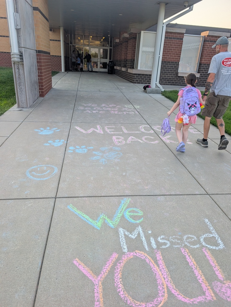 "Welcome Back" and "We missed you" in sidewalk chalk as parents and students walk toward the front of the school