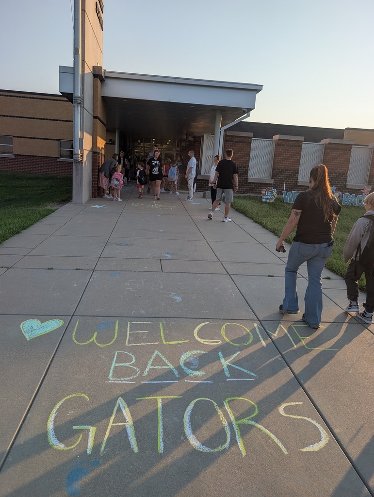 "Welcome Back Gators" in sidewalk chalk as students and parents walk toward the front of the school