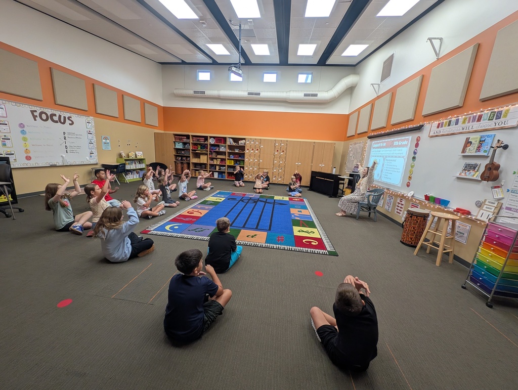 students sitting in a semi circle on the floor doing stretches in the music classroom