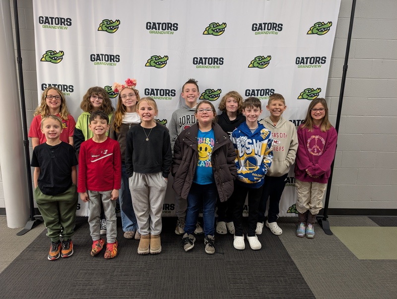 Grandview spelling bee participants pose in front of a backdrop that has the Grandview logo on it.