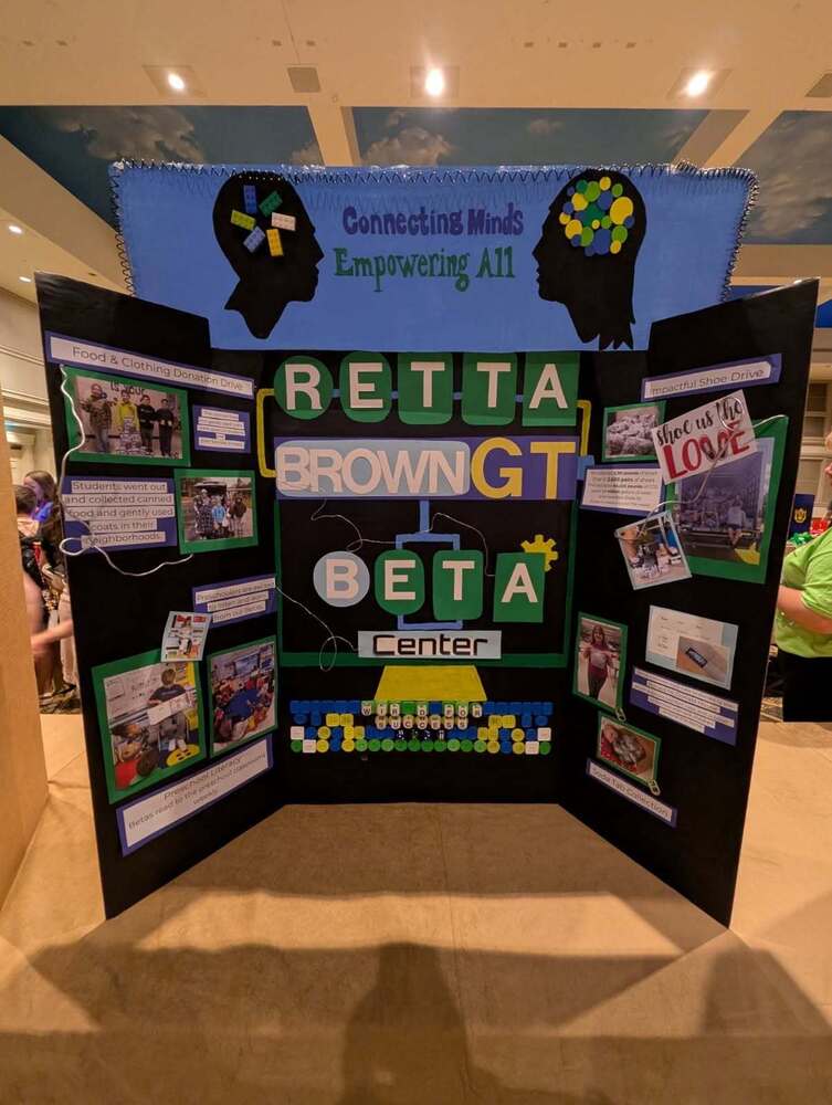 A black tri-fold display board created by Retta Brown GT Beta Center features the message “Connecting Minds, Empowering All.” The board highlights student service projects, including food and clothing donations, a shoe drive, preschool literacy activities and soda-tab collection, using photos, colorful labels and computer-themed decorations.