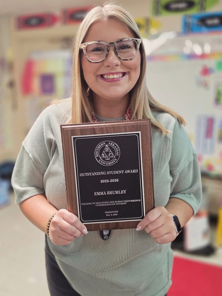 Emma Brumley smiles while holding an Outstanding Student Award plaque from Southern Arkansas University’s College of Education and Human Performance. She is pictured indoors in a classroom setting with a softly blurred background.