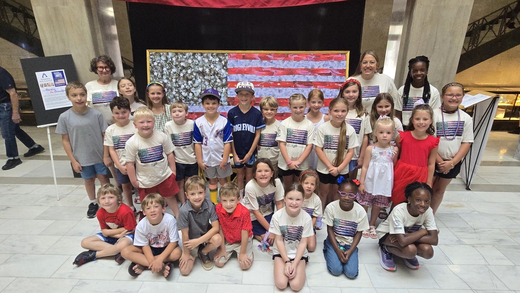 A group of Hugh Goodwin Elementary students and staff pose inside the Union County Courthouse in front of a large student-created American flag artwork following its unveiling ceremony. Many students are wearing matching patriotic shirts in celebration of the project.