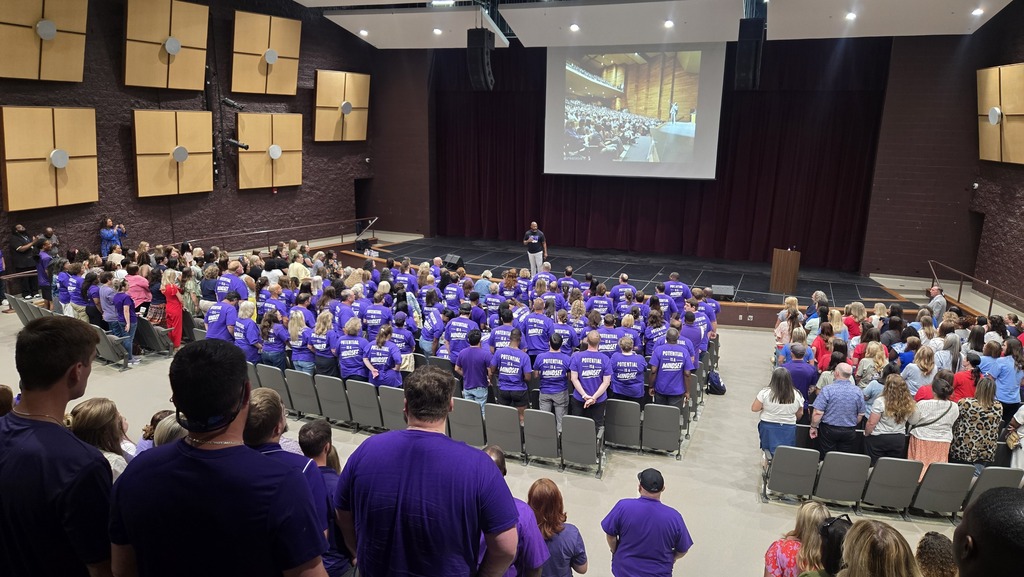 El Dorado School District teachers and staff stand together in a packed auditorium during Opening Session as a speaker addresses the group from the stage. Many staff members are wearing purple shirts featuring the message, βPotential is a Mindset.β