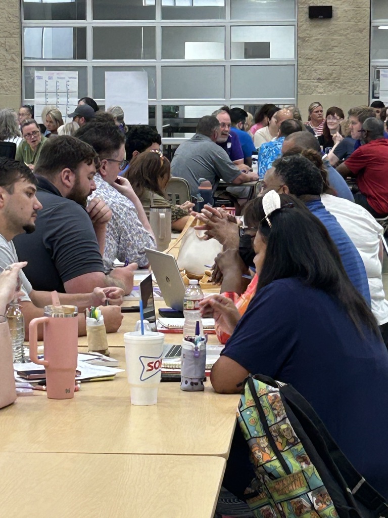 Dozens of El Dorado School District teachers sit in small groups around cafeteria tables, collaborating and discussing literacy strategies during a professional development session for grades 7β12.