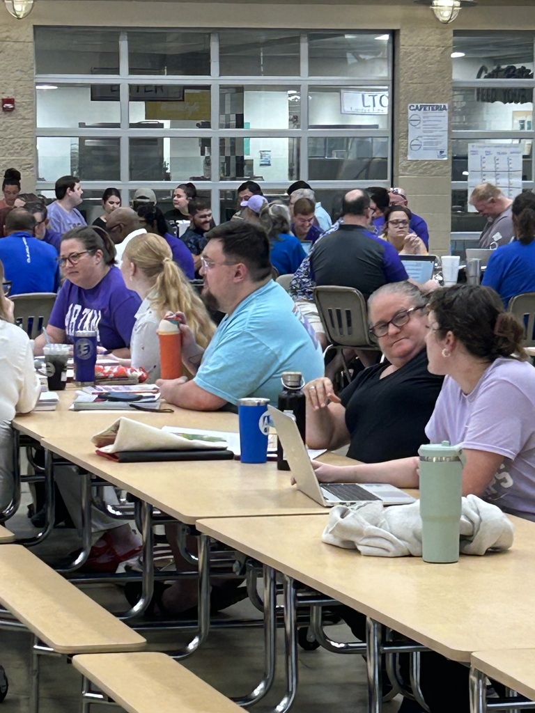 Groups of 7thβ12th grade teachers work together at tables with laptops, notebooks, and instructional materials during a literacy-focused professional development workshop.
