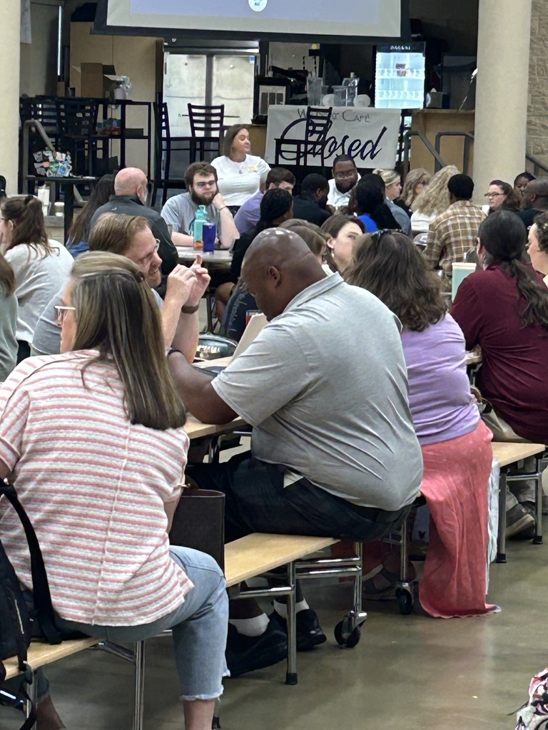 Secondary teachers participate in table discussions during a district professional learning session focused on building stronger readers, with staff members collaborating throughout the cafeteria.