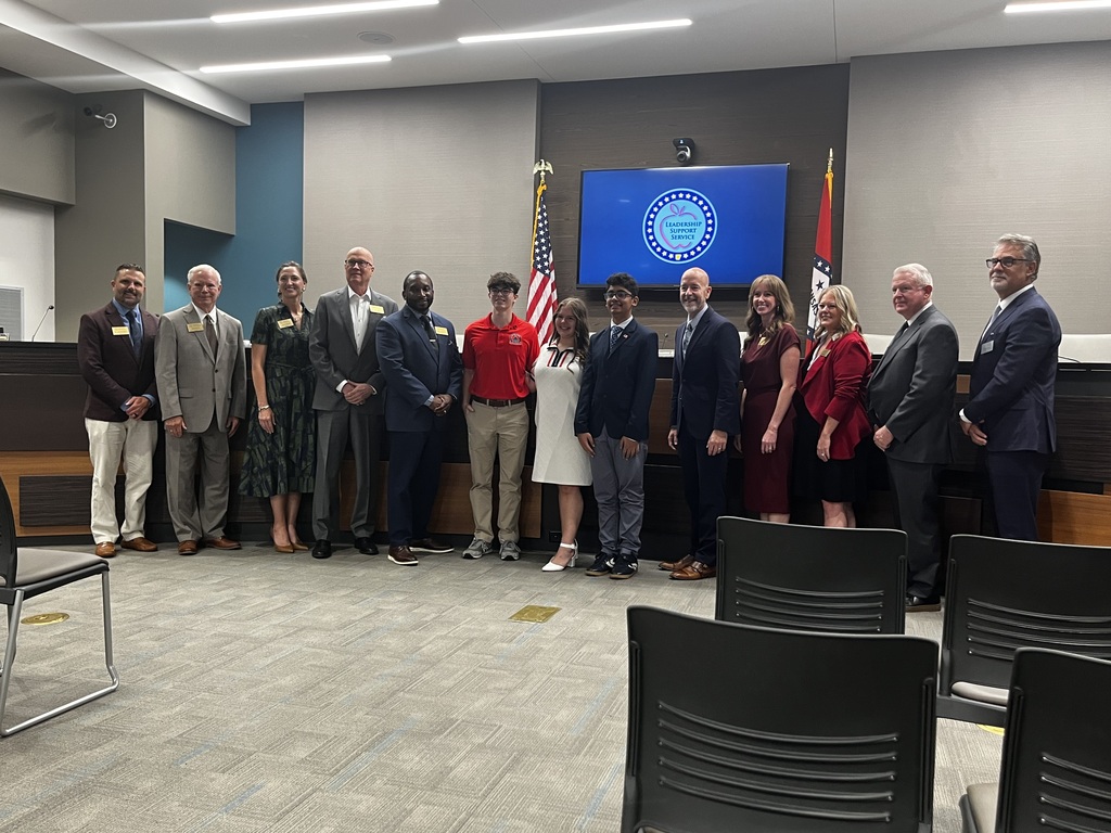A Barton Junior High School student stands with Arkansas education officials and fellow Civics Bee participants during recognition at the Arkansas State Board of Education meeting. The group poses together in the board room in front of the U.S. and Arkansas flags.