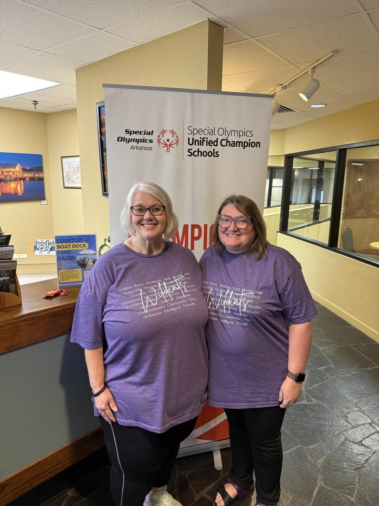 Two El Dorado School District educators wearing matching purple shirts pose on either side of a Special Olympics Arkansas Unified Champion Schools banner that reads “Champions Together.”
