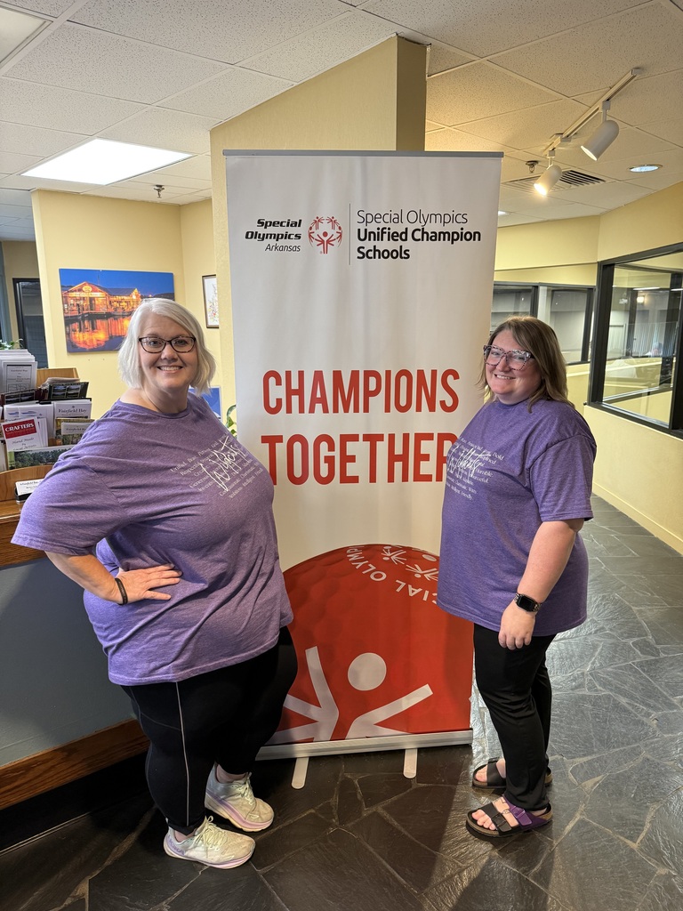 Two El Dorado School District educators in matching purple shirts smile together in front of a Special Olympics Arkansas Unified Champion Schools “Champions Together” banner at the Champions in the Classroom Conference.