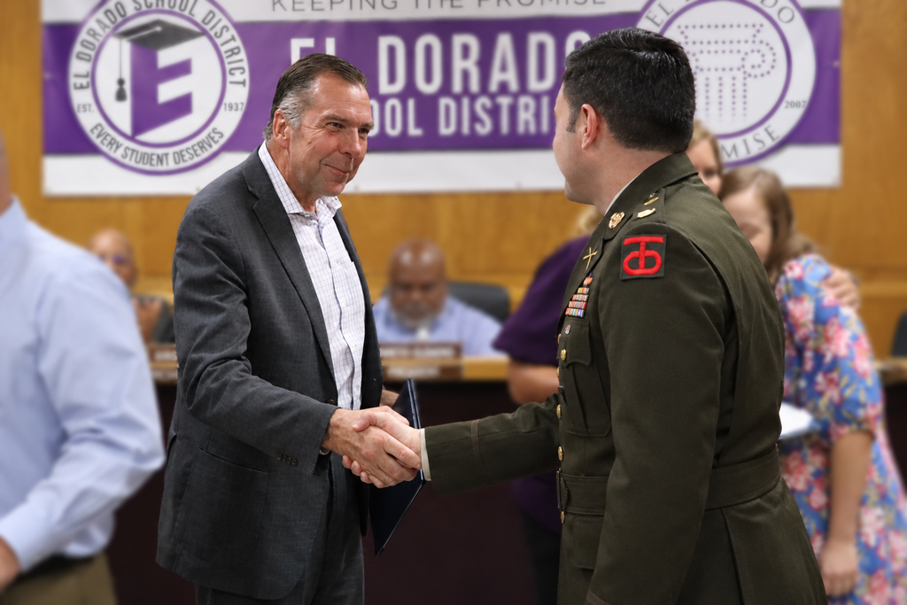 An El Dorado School District administrator shakes hands with a uniformed service member after receiving an ESGR Patriot Award during the School Board meeting. The El Dorado School District banner is visible in the background.