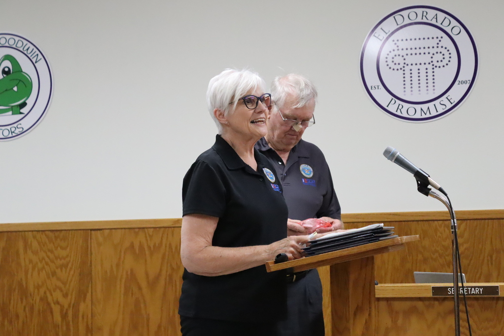 An ESGR volunteer speaks at the podium during the El Dorado School Board meeting while another ESGR representative stands behind her. Several Patriot Award certificates are resting on the podium.