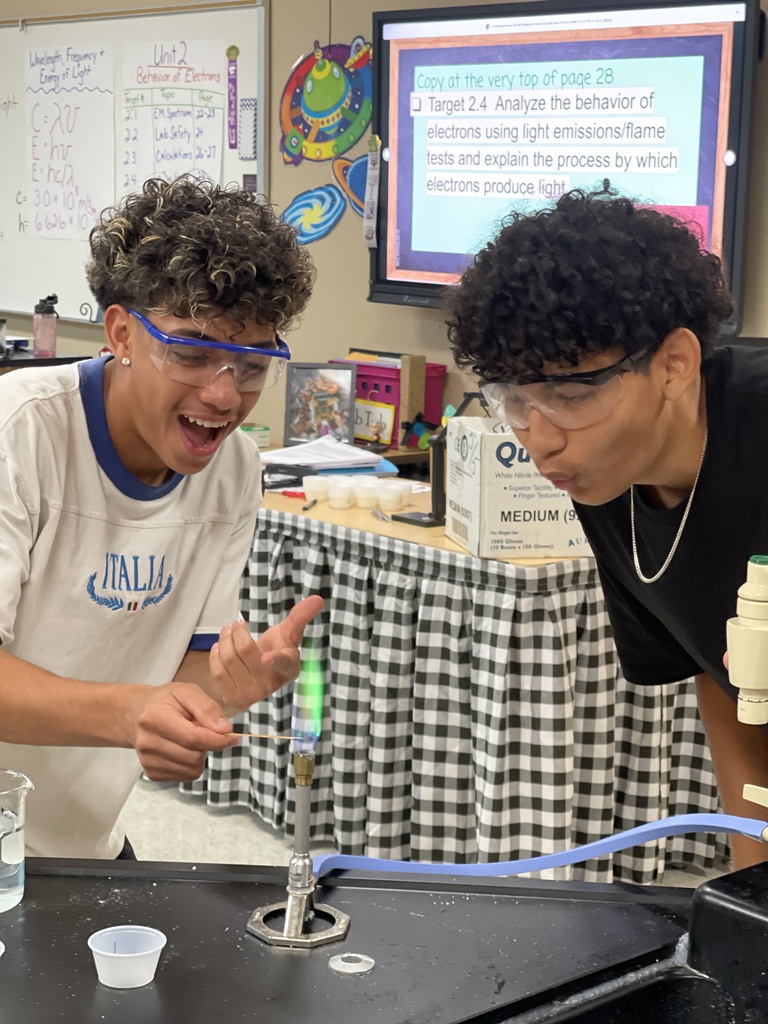 Two Advanced Chemistry students react enthusiastically as they observe a bright green flame during a flame test experiment in the chemistry lab.